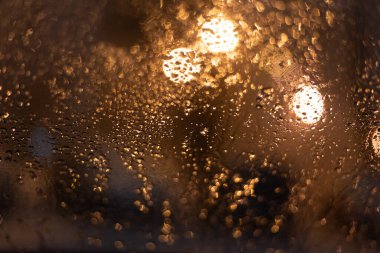 Yağmur damlaları ve ışıklarla bulanık arkaplan.