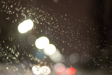 Yağmur damlaları ve ışıklarla bulanık arkaplan.