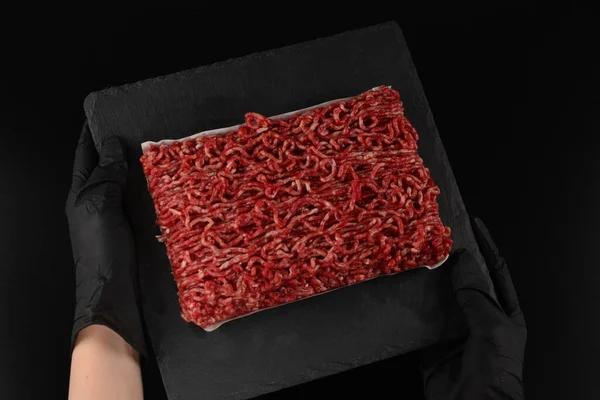 Chopped raw meat  on a black  background in woman hands.