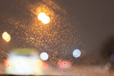 Yağmur damlaları ve ışıklarla bulanık arkaplan.