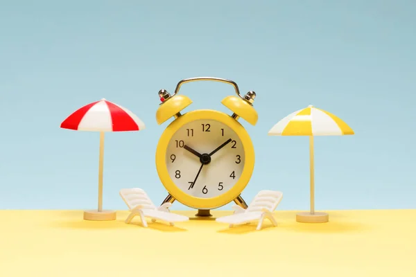 Time to travel. Sun lounger, yellow umbrella and alarm clock on a yellow, blue background.