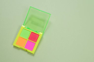 Yeşil arka planda mor, yeşil, turuncu ve mavi göz farı paleti. Makyaj. Neon renkleri.