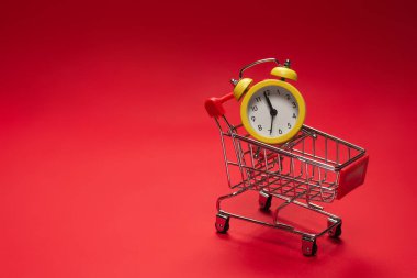 Alışveriş zamanı. Kırmızı arka planda alışveriş sepetindeki sarı alarm saati. Boşluğu kopyala. 