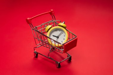 Alışveriş zamanı. Kırmızı arka planda alışveriş sepetindeki sarı alarm saati. Boşluğu kopyala. 
