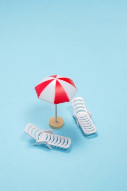 Seyahat konsepti. Güneş şezlongu, mavi arka planda kırmızı şemsiye. Boşluğu kopyala. 