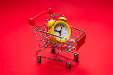Alışveriş zamanı. Kırmızı arka planda alışveriş sepetindeki sarı alarm saati. Boşluğu kopyala. 