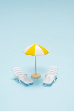 Seyahat konsepti. Güneş şezlongu, mavi arka planda sarı şemsiye. Boşluğu kopyala. 