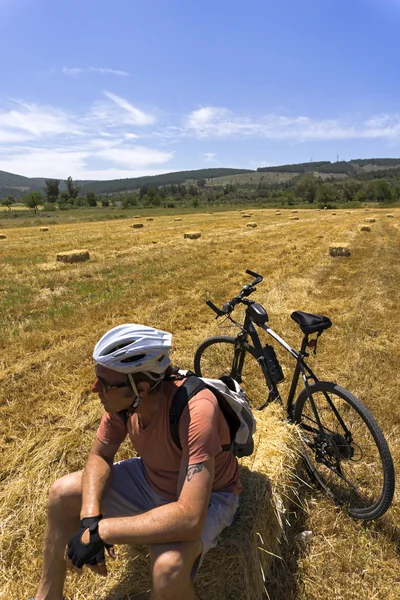 Cyclist man is resting on hay bale in a field — Stock Photo, Image