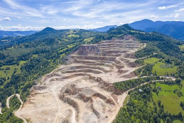 Çimento ocağı, kaya terasları ve çalışan kamyonların hava manzarası.