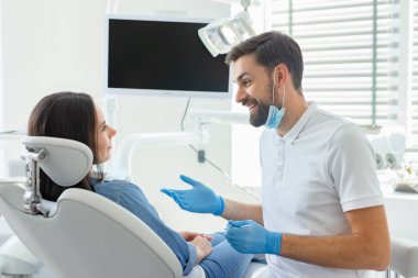 side view of dentist advicing and gesturing to patient in modern clinic clipart