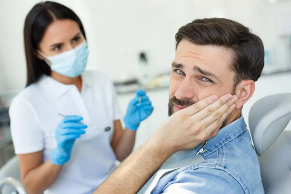 upset patient touching face while having toothache near dentist