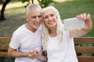 Akıllı telefon tutan ve kocasıyla selfie çeken mutlu olgun bir kadın.