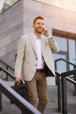 Resmi takım elbiseli neşeli adam cep telefonu kullanıyor ve açık merdivenlerde sohbet ediyor.
