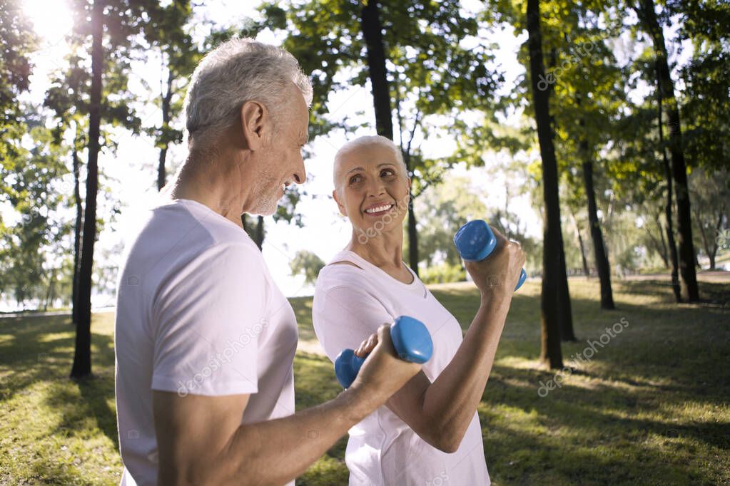Cheerful mature lady looking at her husband while exercising outdoors