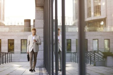 Klasik takım elbiseli başarılı bir iş adamı akıllı telefonuna dikkatle bakarken dışarıda yürüyor.