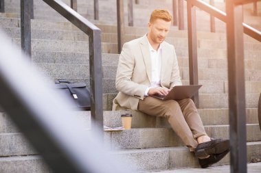 Açık hava basamaklarında otururken internet üzerinden iletişim kuran özenli zeki bir adam.