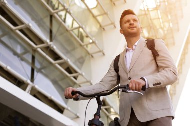 Gülümseyen zarif bir adam yana bakıyor ve bisikletinin gidonunu tutuyor.