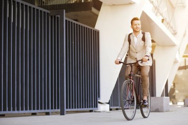 Şık takım elbiseli çekici bir adam sokakta bisiklet sürüyor ve bakışlarını kaçırıyor.