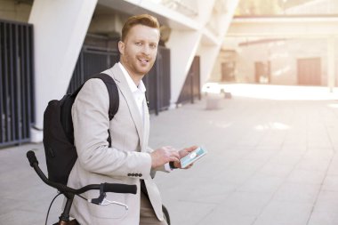 Yakışıklı iş adamı bisikletine yaslanırken tabletine bir mesaj alıyor.