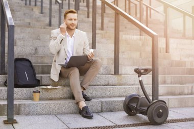 Klasik takım elbiseli karizmatik bir adam dizlerinin üstüne çöküp kulaklıklarını takıyor.