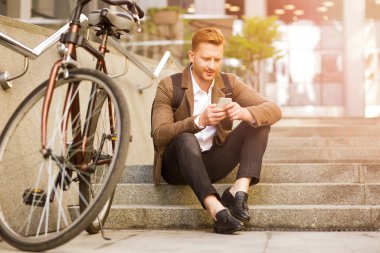 Merdivenlerde dinlenen ceketli ve cep telefonuna mesaj atan dikkatli bir adam.