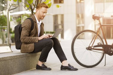 Sınırda oturan ve yeni bir proje üzerinde çalışırken dizüstü bilgisayar kullanan odaklanmış stil sahibi bir adam.