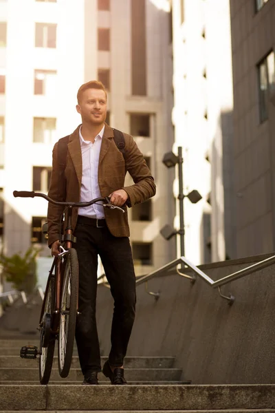 Positive man in classic clothes looking away while holding his bicycle