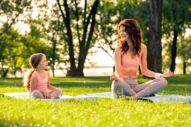 Lotus 'ta oturan kadın ve küçük kız parkta birlikte poz veriyorlar.