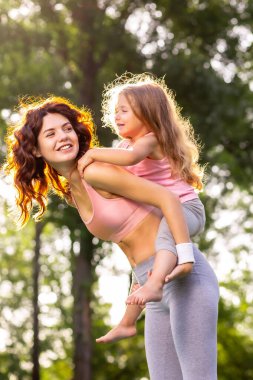 Kızı sırtında gülen annesine parkta biniyor.