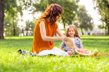 Anne ve tatlı kız piknik battaniyesinde oturup yemek hazırlıyorlar.