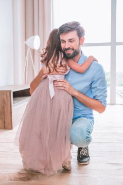 Gülümseyen baba oturma odasında kızını kucaklıyor.