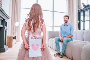 Baba evdeki kanepede otururken, küçük kız kalbinin fotoğrafını sırtında taşıyor.