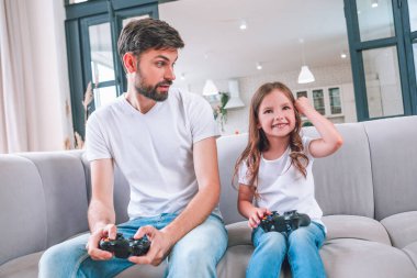 Küçük kız evde babasıyla birlikte kanepede oturuyor.