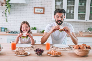 Baba ve kız masada oturup sandviçlere bakıyorlar.
