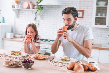 Küçük kız babasıyla mutfakta meyve suyu içiyor.