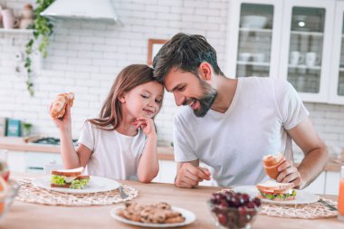 Baba ve kızı mutfakta birlikte kahvaltı ediyorlar.
