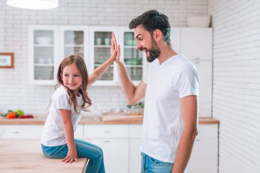 Kızım mutfaktaki masada oturan babasına beşlik çakıyor.