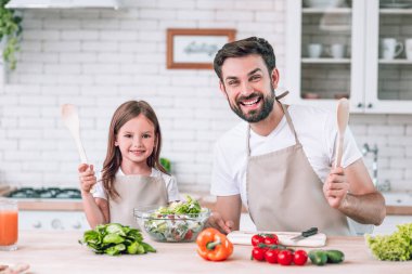 Gülümseyen baba ve kızın portresi. Mutfakta salata hazırlarken ve kameraya bakarken.