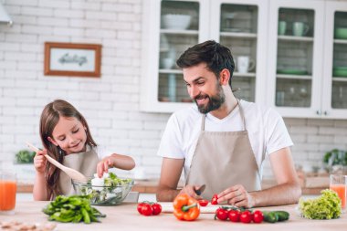 Baba kızına bakıyor ve mutfakta salata hazırlıyor.