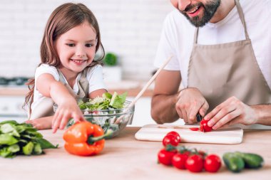 Baba kızıyla birlikte domates doğruyor mutfak masasının yanında oturuyor.