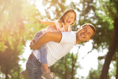 Mutlu kız, güneşli bir günde parkta babasını sırtında taşıyor.
