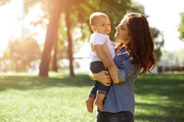 Güneşli bir günde parkta çocuğu tutan kadın.