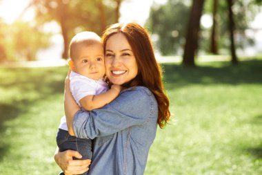 Anne oğlunu kucaklıyor, parkta ellerini tutuyor.