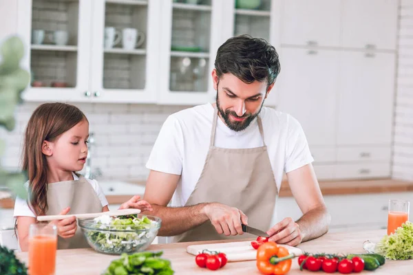 daddy slicing tomatoes with daughter looking sitting near at the kitchen table