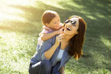 Sırtından sarılan kızıyla kağıt maske takan gülümseyen bir anne.
