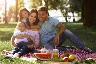 Kız, anne ve babasına sarılıyor erkek, annesinin kucağında oturuyor ve parktaki kameraya bakıyor.