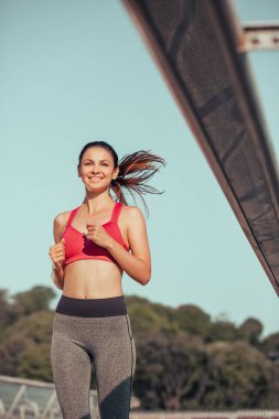 Güler yüzlü esmer sporcu gündüz şehirde koşuyor.