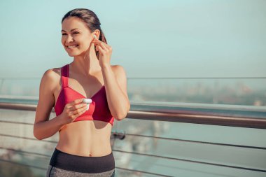 Şehirde koşmak için kulaklık takan gülümseyen kadın koşucunun portresi.