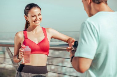 Antrenör ve atlet ellerinde su şişeleri tutarken konuşuyor.
