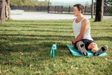 Genç adam parkta paspasın üzerinde egzersiz yapıyor.